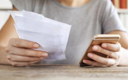 Persona sujeta un teléfono y una factura. Persona sujeta un teléfono y una factura.