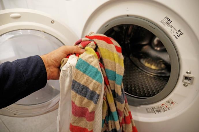 Una persona introduce ropa sucia en una lavadora.