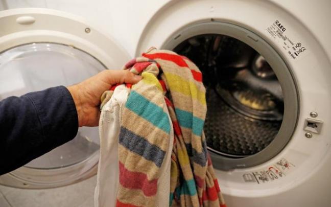 Una persona introduce ropa sucia en una lavadora.