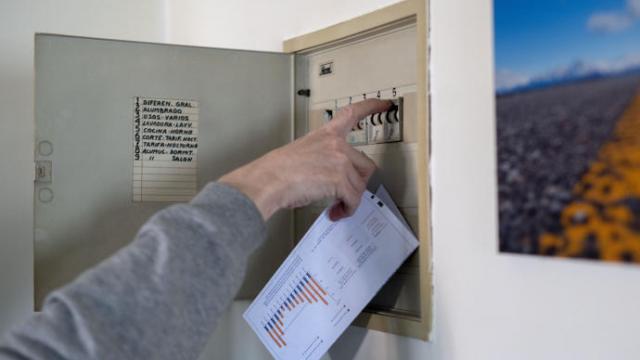 Un hombre sube los plomos de la luz con una factura de luz en la mano