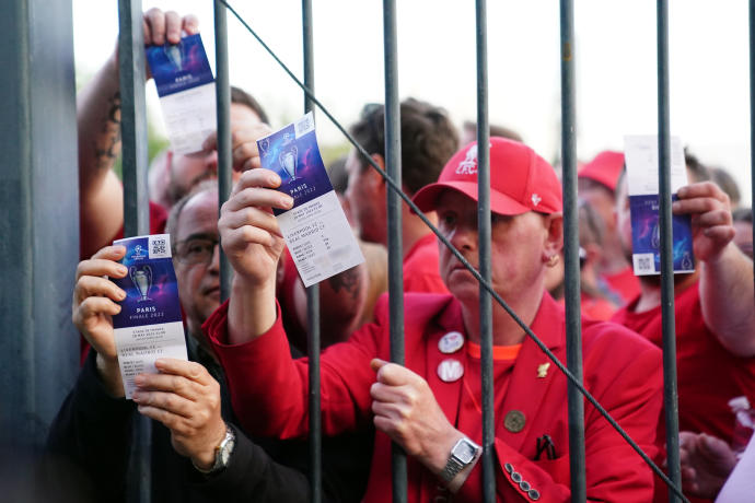 Los aficionados del Liverpool se quedan fuera del estadio mientras muestran sus entradas.