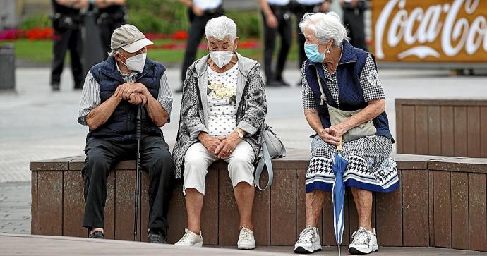 Tres personas mayores, protegidas con mascarilla, charlan en un banco, ayer en Donostia. Foto: Juan Herrero / Efe