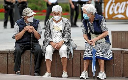 Tres personas mayores, protegidas con mascarilla, charlan en un banco, ayer en Donostia. Foto: Juan Herrero / Efe