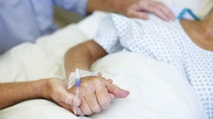 Un familiar agarrando la mano de un paciente enfermo.