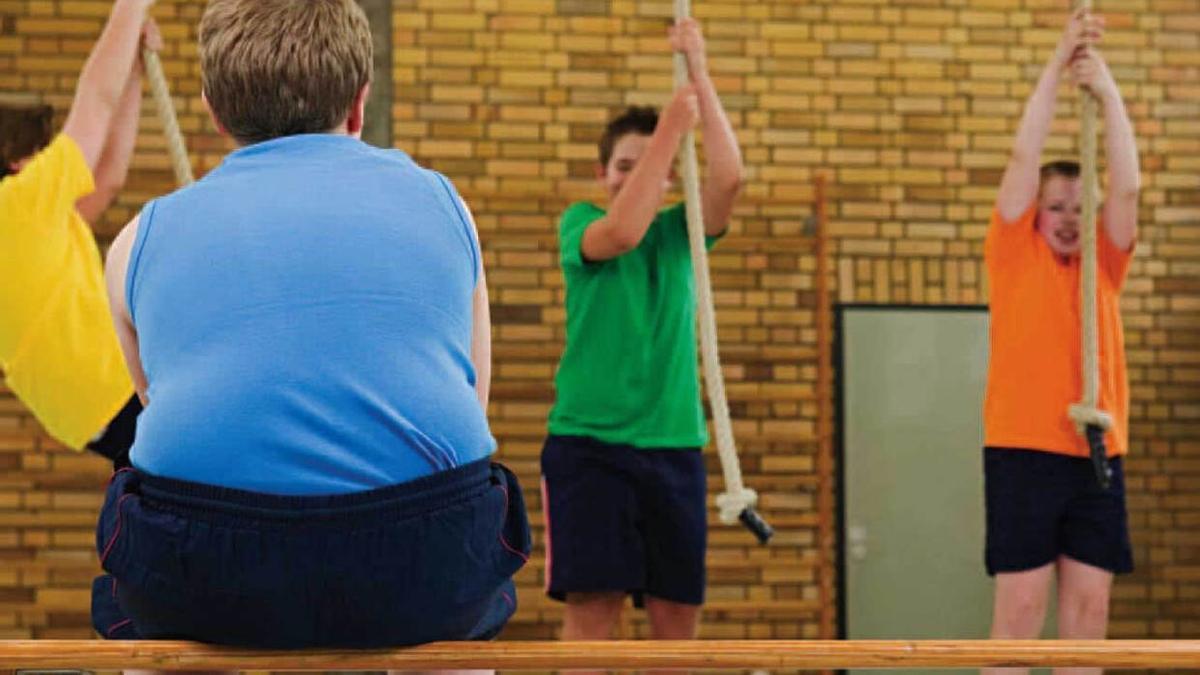 Un niño obeso observa a sus compañeros en clase de gimnasia.