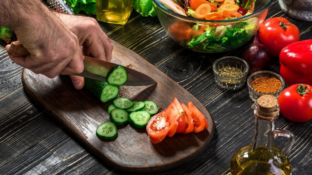 Un hombre corta pepino y tomate para preparar una ensalada.