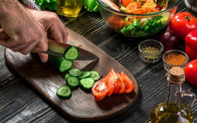 Un hombre corta pepino y tomate para preparar una ensalada.