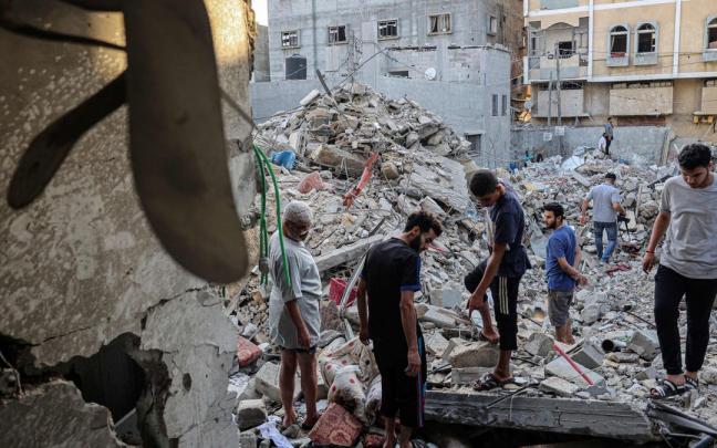 Varios palestinos caminan entre los escombros de un edificio destruido