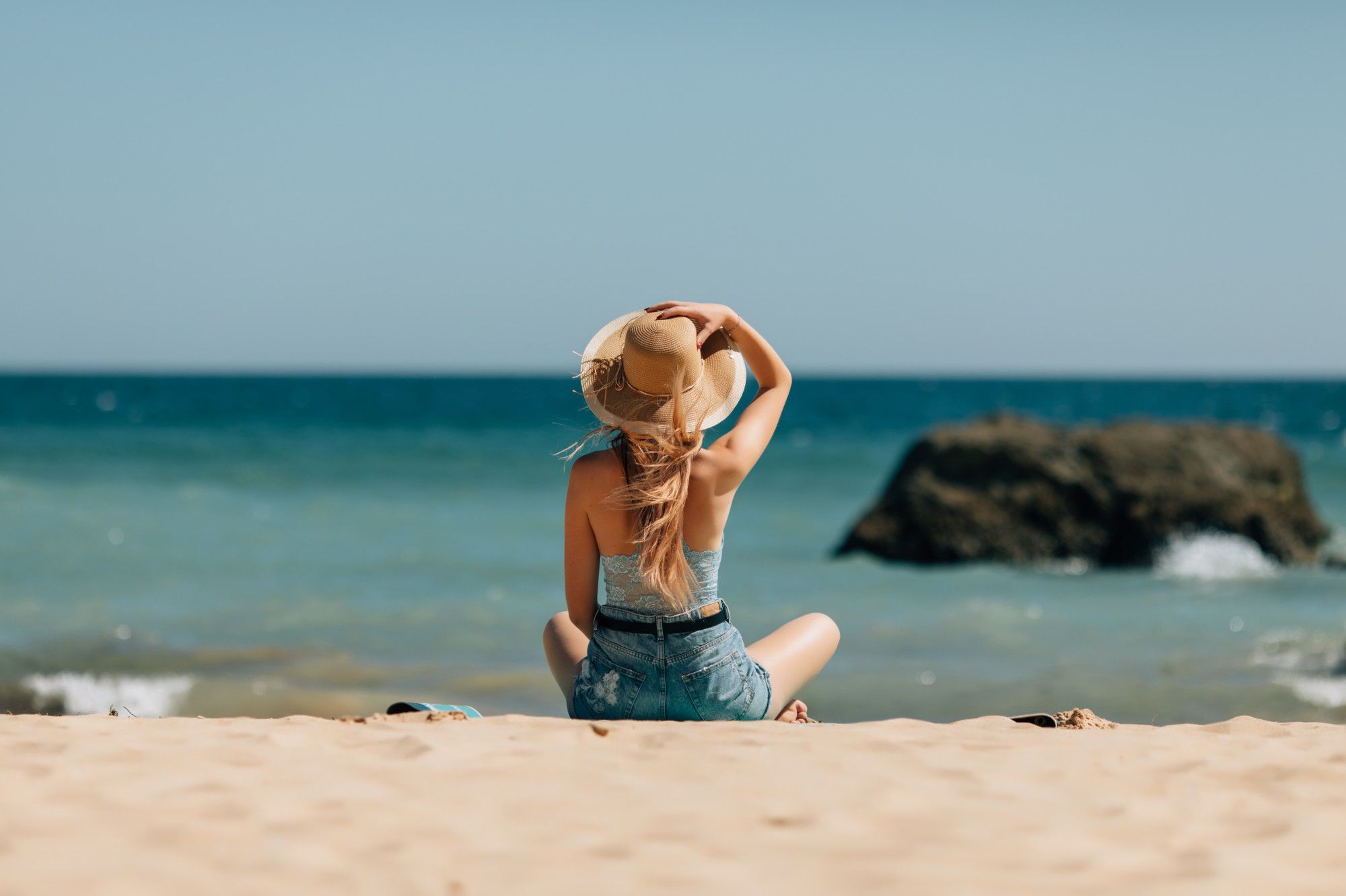 Una mujer se protege la cabeza con un sombrero en la playa.