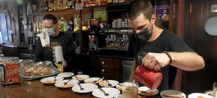 Un camarero prepara un café en un bar de Vitoria mientras su compañero manipula unas tazas. Foto: Alex Larretxi