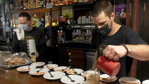 Un camarero prepara un café en un bar de Vitoria mientras su compañero manipula unas tazas. Foto: Alex Larretxi