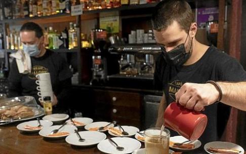 Un camarero prepara un café en un bar de Vitoria mientras su compañero manipula unas tazas. Foto: Alex Larretxi