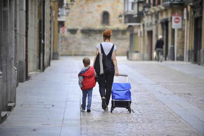 Una mujer, tirando del carro de la compra, y un niño caminan por las calles del Casco Viejo de Bilbao.