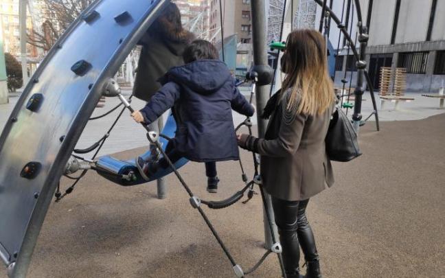 Una mujer cuidando de dos niños en un parque infantil.