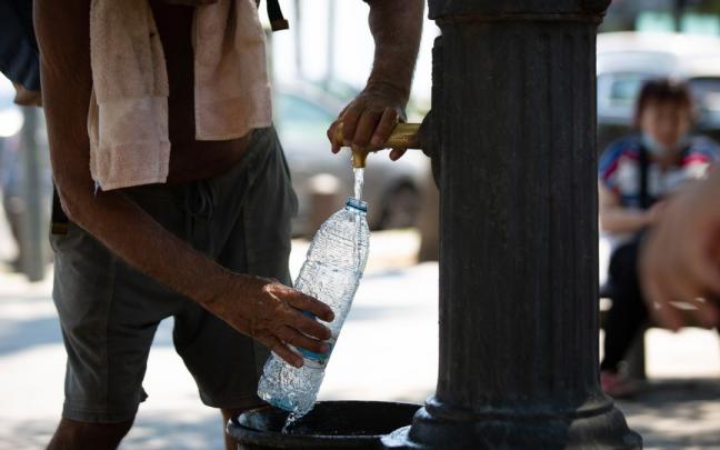 Un hombre rellena una botella de agua en una fuente en plena ola de calor. Un hombre rellena una botella de agua en una fuente en plena ola de calor.