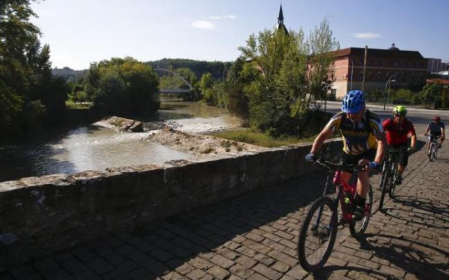 Ciclistas cruzando el puente de Santa Engracia. Detrás, la presa, rota y, al fondo, el puente de Oblatas.