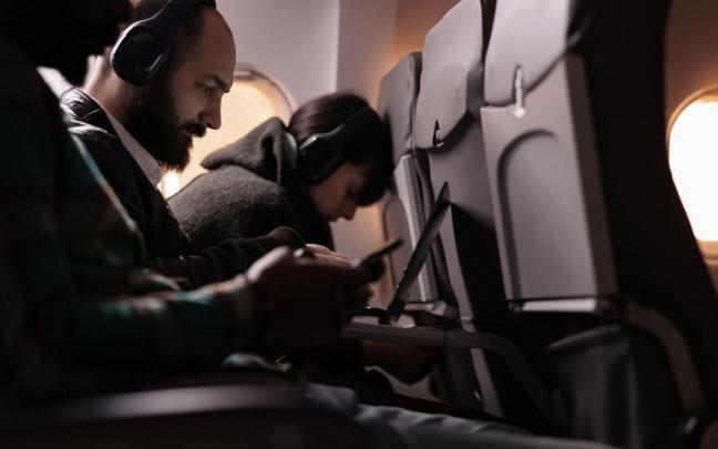 Varias personas con dispositivos electrónicos en un avión. Varias personas con dispositivos electrónicos en un avión.