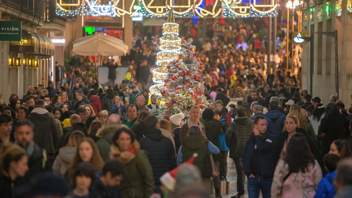 Cientos de personas pasean por una calle muy iluminada de Navidad, haciendo sus compras.