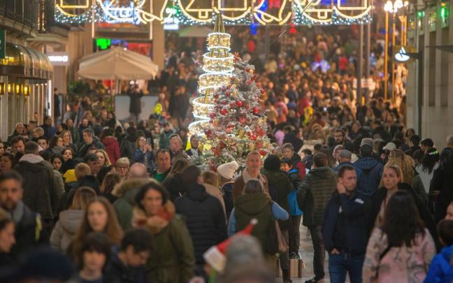 Cientos de personas pasean por una calle muy iluminada de Navidad, haciendo sus compras.
