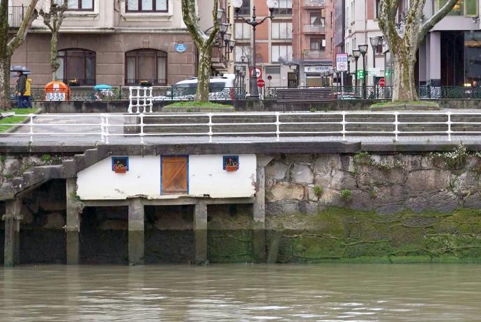 La caseta a ras de Ría en el Campo Volantín de Bilbao y la fachada del hotel Hesperia hacen juego a la luz del día.