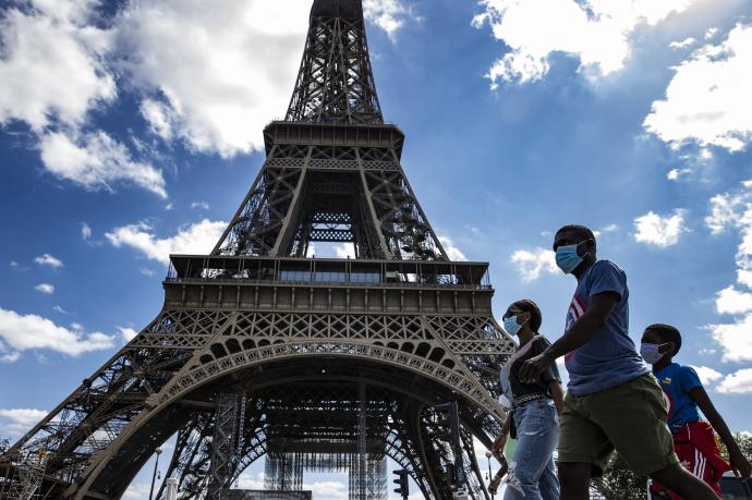 Varias personas con mascarilla junto a la Torre Eiffel en París