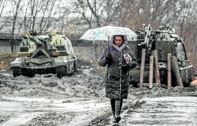 Una mujer camina frente a blindados rusos preparados para la invasión en los límites de Rusia con Ucrania. Foto Efe