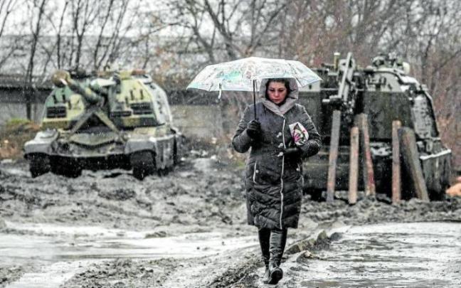 Una mujer camina frente a blindados rusos preparados para la invasión en los límites de Rusia con Ucrania. Foto Efe