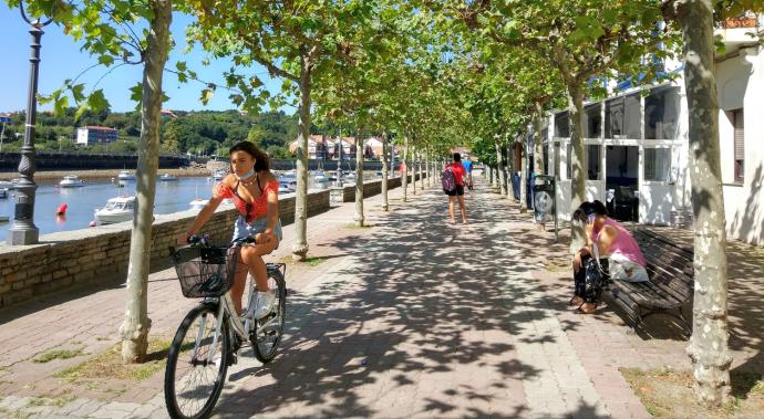 Una joven, en bicicleta entre las sombras de los árboles por el paseo de la ría.