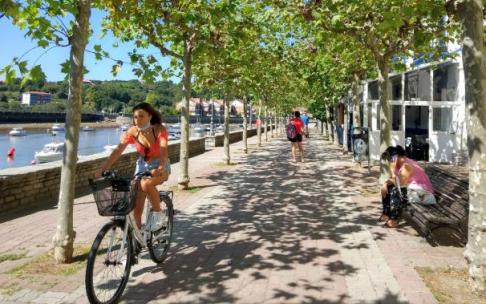 Una joven, en bicicleta entre las sombras de los árboles por el paseo de la ría.