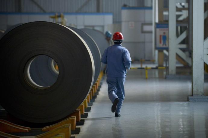 Un trabajador pasa en una acería junto a unas bobinas de acero.