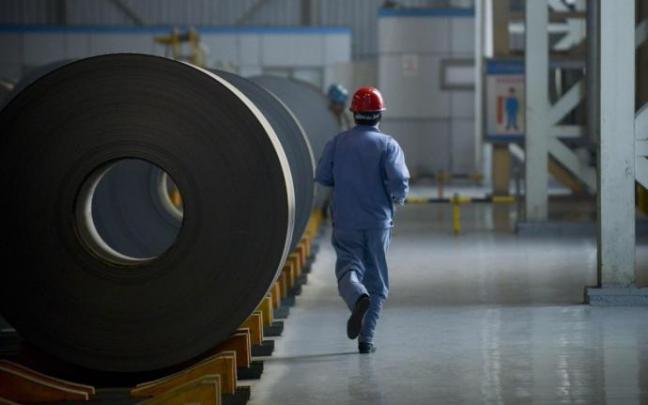 Un trabajador pasa en una acería junto a unas bobinas de acero.