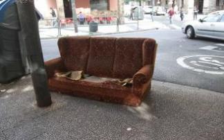 Un sofá viejo tirado al lado de un contenedor.