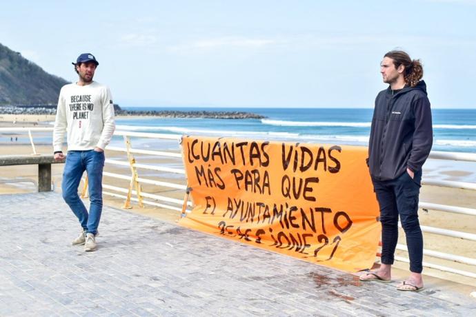 Dos surfistas junto a una pancarta para pedir más seguridad en el agua.