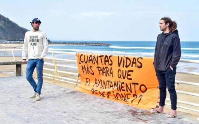 Dos surfistas junto a una pancarta para pedir más seguridad en el agua.
