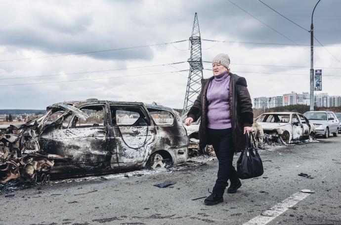 Una mujer camina junto a los coches destrozados por los bombardeos en Irpin, ciudad cercana a Kiev