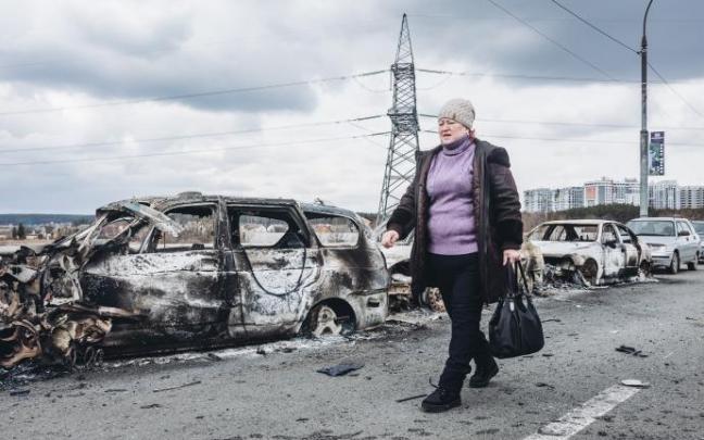 Una mujer camina junto a los coches destrozados por los bombardeos en Irpin, ciudad cercana a Kiev