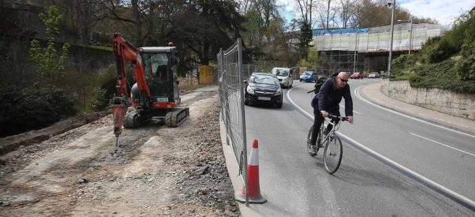 Un ciclista desciende por la cuesta del Labrit, donde se observa la maquinaria utilizada para habilitar el nuevo carril bici y al fondo, la pasarela en reparación.