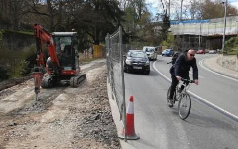 Un ciclista desciende por la cuesta del Labrit, donde se observa la maquinaria utilizada para habilitar el nuevo carril bici y al fondo, la pasarela en reparación.