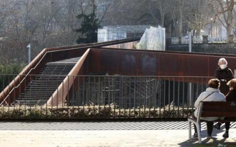 Varias mujeres sentadas frente a la pasarela del Labrit, donde son visibles los andamios colocados.