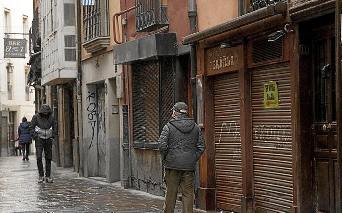 Viandantes paseando junto a un bar cerrado durante el confinamiento. Foto: Josu Chavarri