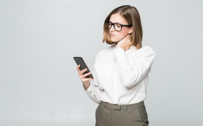 Una mujer presenta dolor de cuello mientras mira el móvil.