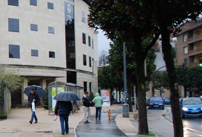Personas andando con paraguas junto al Ayuntamiento de Llodio