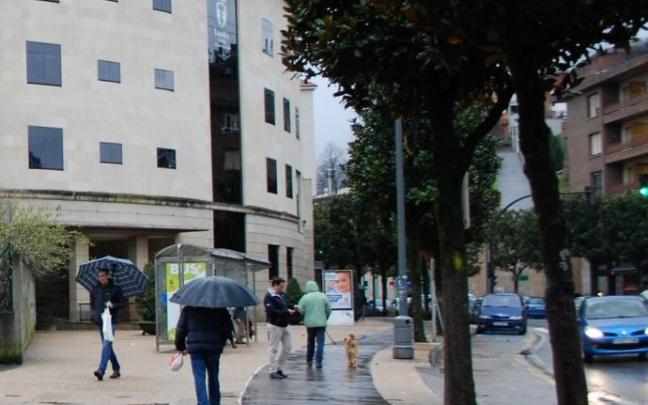 Personas andando con paraguas junto al Ayuntamiento de Llodio
