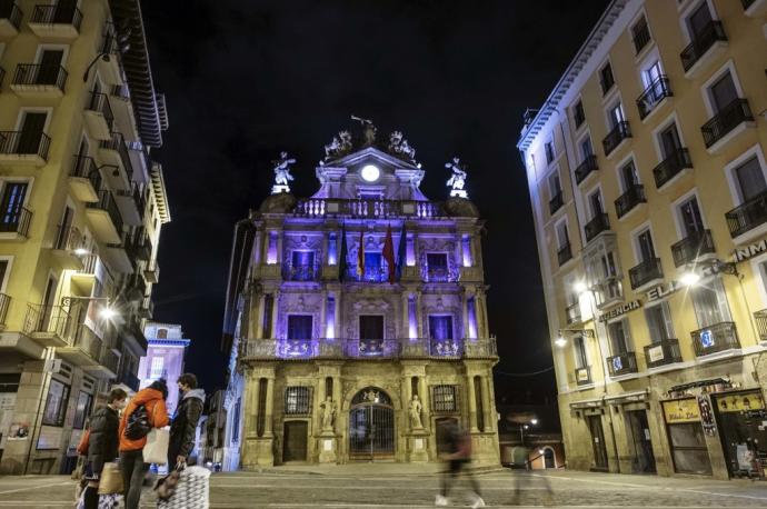 Fachada del ayuntamiento de Pamplona de noche e iluminada de color morado con motivo de la celebración del 8M, Día Internacional de la Mujer.