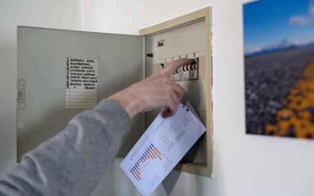 Un hombre sube los plomos de la luz con una factura de luz en la mano.