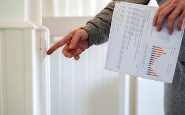 Un hombre enciende un interruptor con una factura de luz en la mano.