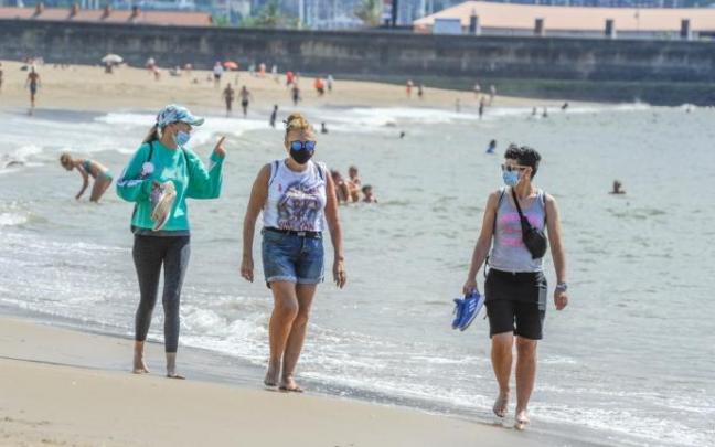 Varias personas pasean por la playa con mascarilla. Varias personas pasean por la playa con mascarilla.