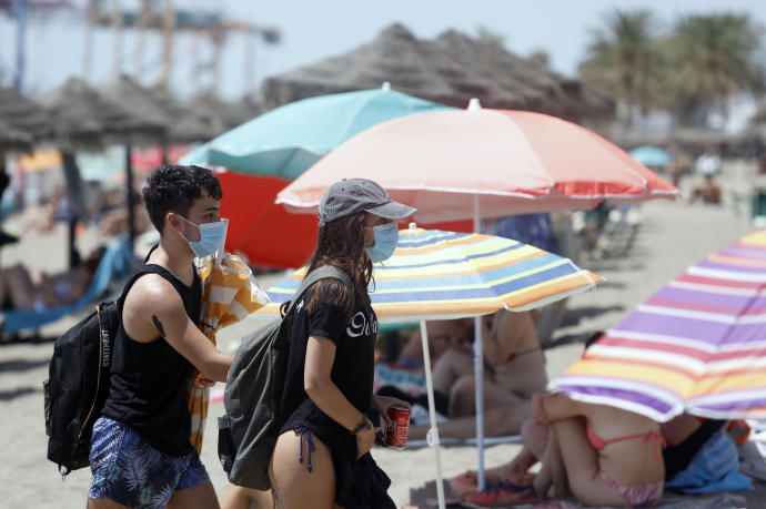 Dos personas con mascarillas mientras pasan entre sombrillas en la playa de La Malagueta.