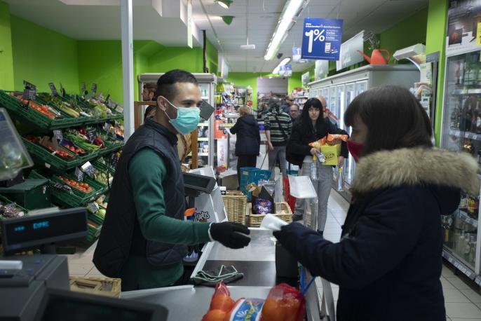 Un cajero en un supermercado atiende con mascarilla.