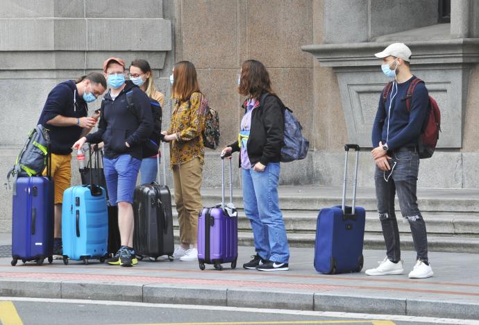 Varios viajeros esperan al autobús con sus maletas y mascarillas.